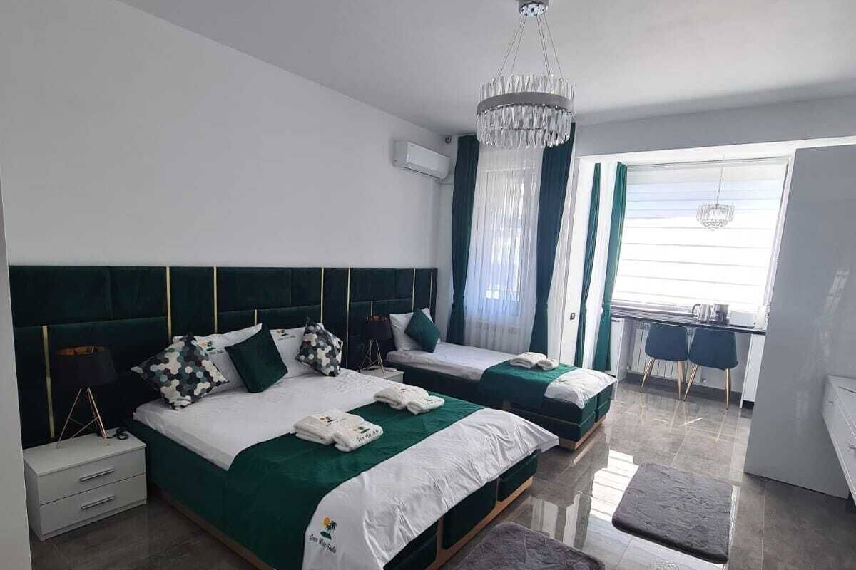 A modern bedroom with a large bed, two smaller beds, a chandelier, and a view of the kitchen.
