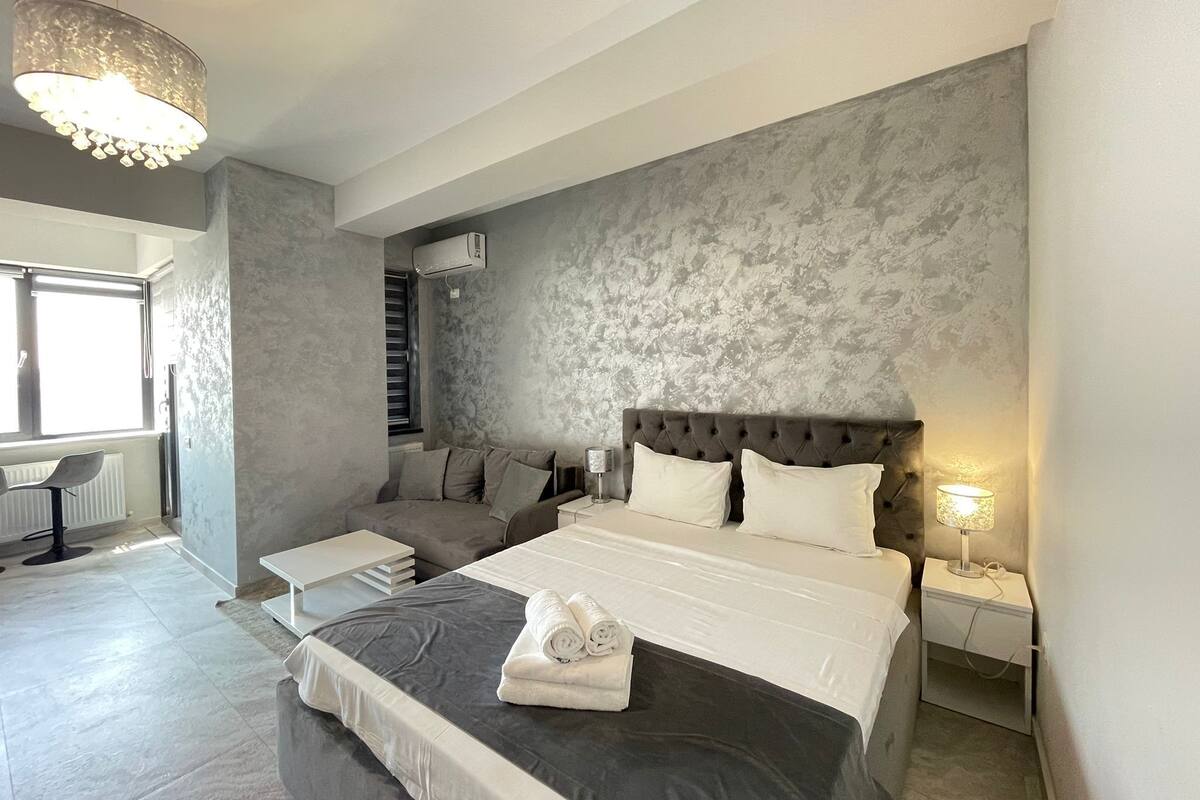 A modern bedroom with a large bed, a tufted headboard, and a grey textured wall.