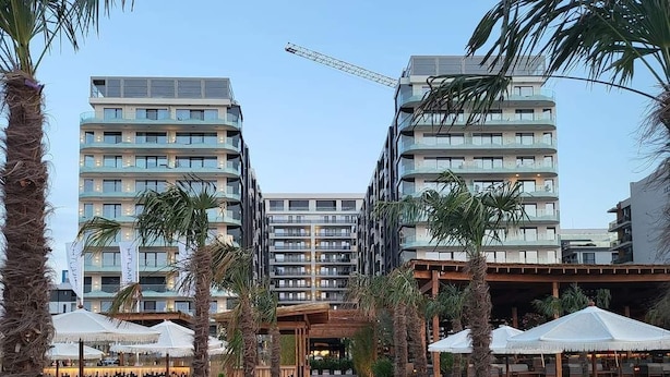 Un sendero conduce a un edificio con varios balcones, rodeado de palmeras y tumbonas.