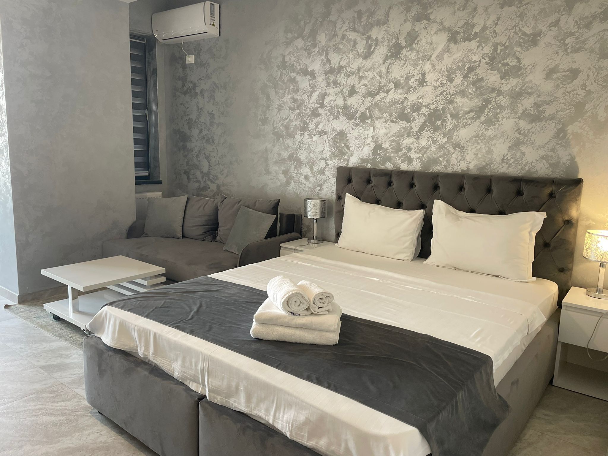 A modern bedroom with a large bed, grey upholstered headboard, and a grey sofa.