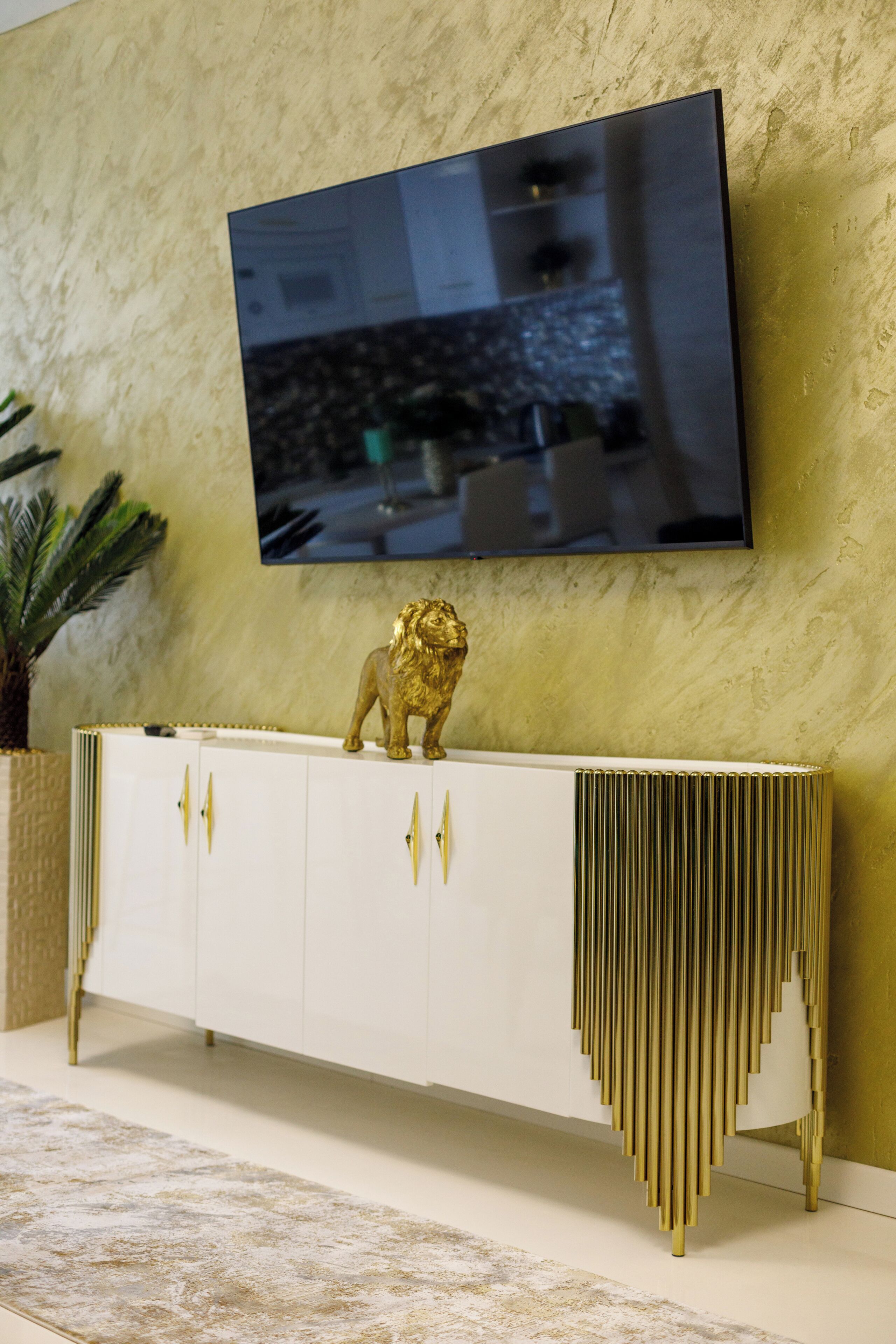 A modern living room with a mounted flat-screen TV, a white console with gold accents, and a decorative golden lion statue.