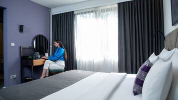 A hotel room with a bed, a desk, a chair, a computer, and a window with curtains.