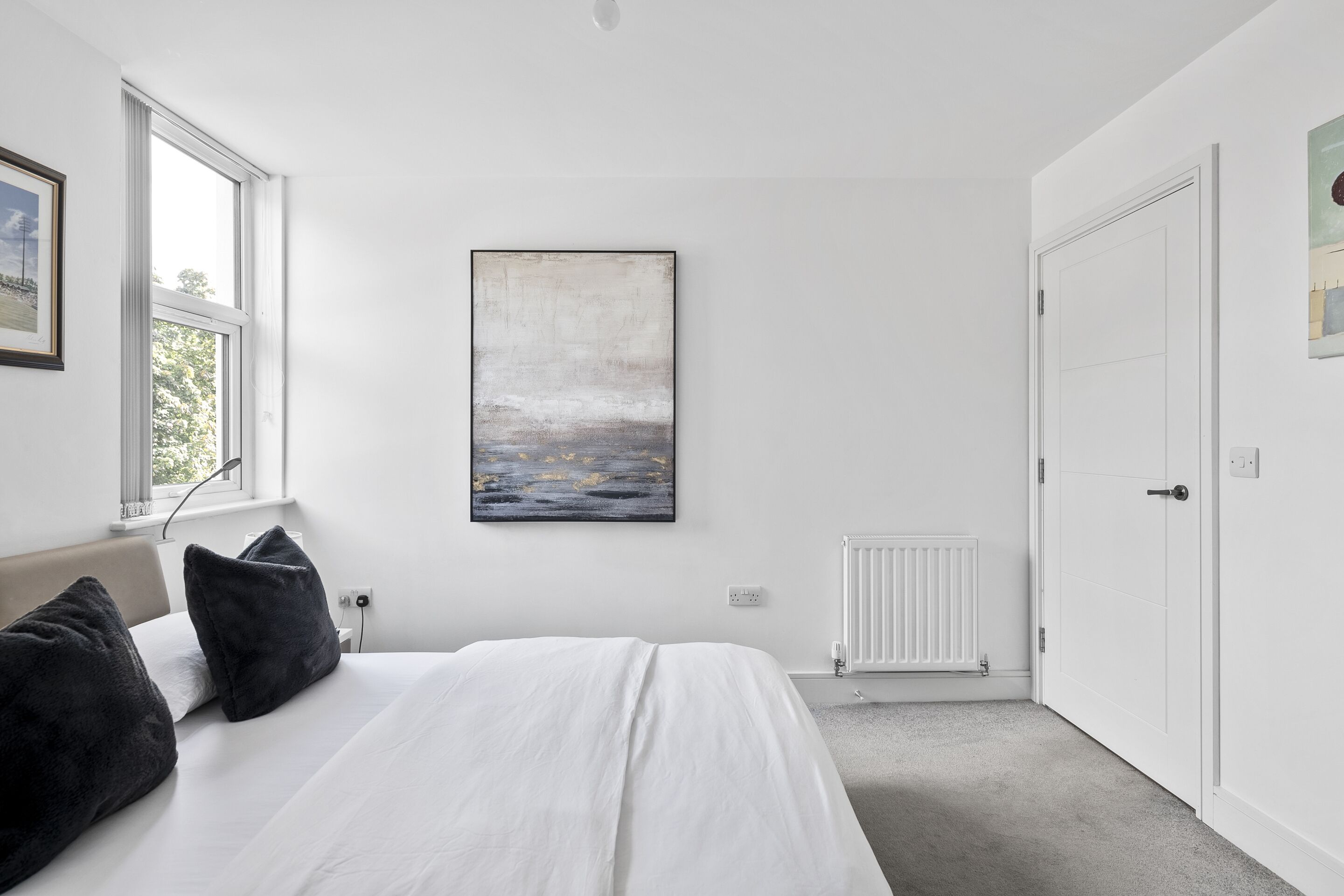 Un dormitorio con cama, ventana, radiador y puerta.