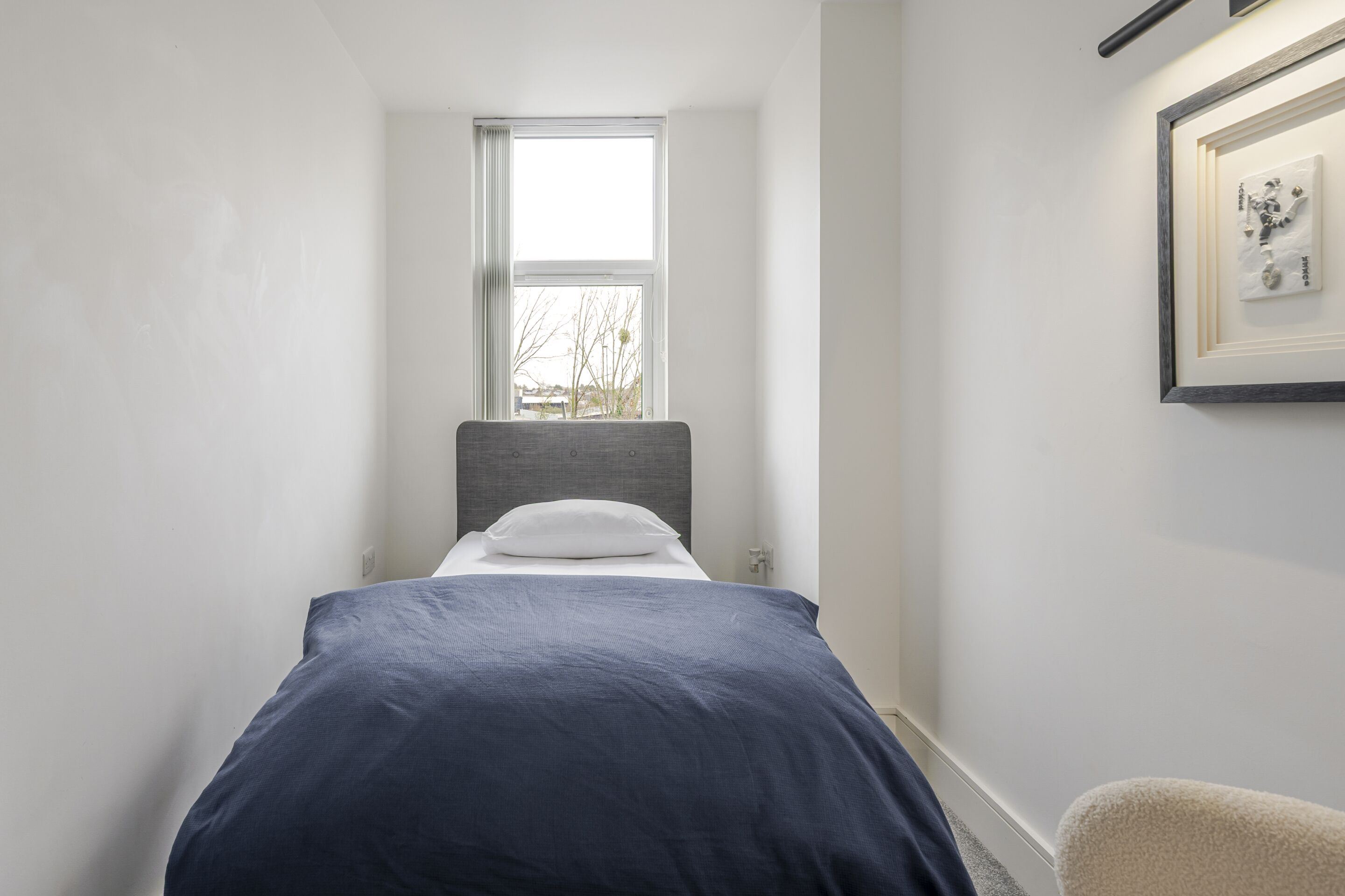 A narrow room with a bed, a window, and a framed picture on the wall.