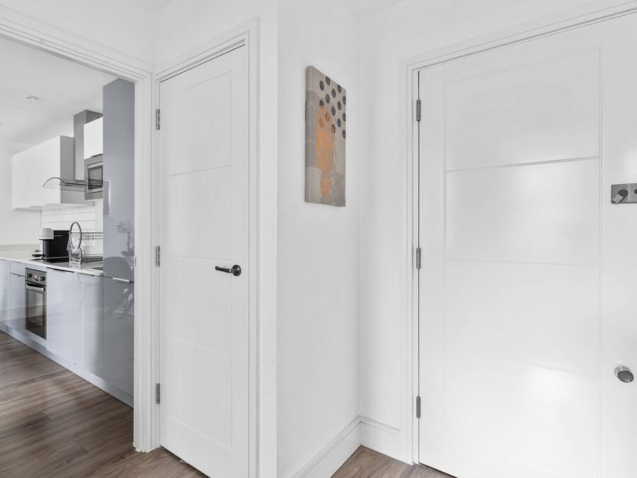 Una cocina moderna con electrodomésticos de acero inoxidable, una encimera blanca y suelo de madera.