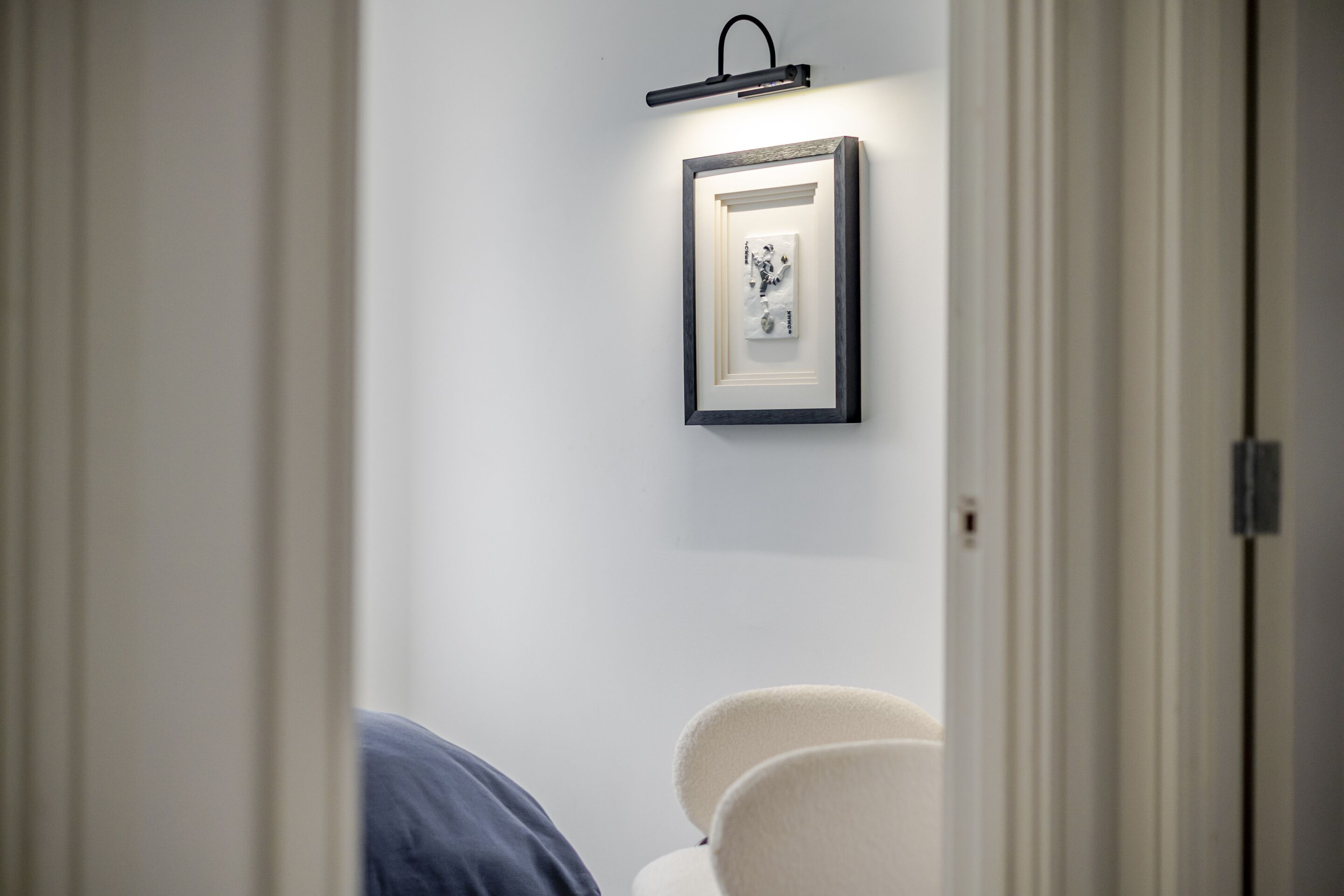 A doorway leading into a room with a framed artwork on the wall and a bedside table with a lamp.