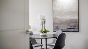 Un comedor con una mesa redonda, dos sillas y un jarrón con flores blancas.