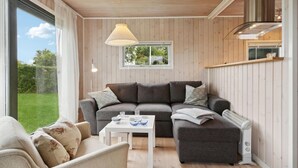 A modern living room with a sectional sofa, a small white table, and a large window offering a view of the outdoors. - 2 bedroom stunning home in Otterup (Otterup)