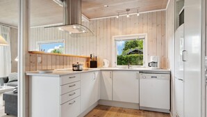 A modern kitchen with white cabinets, a wooden countertop, a built-in dishwasher, and a window offering a view of greenery. - 2 bedroom stunning home in Otterup (Otterup)