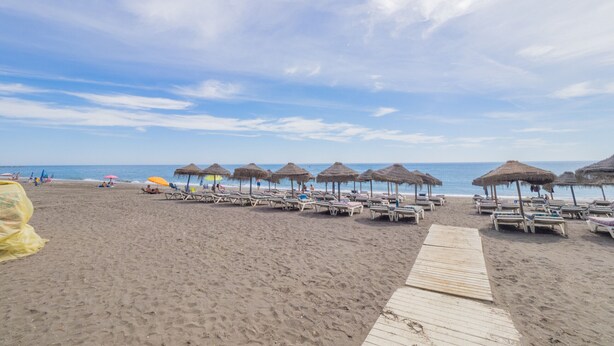 A beach with rows of sun loungers and thatched umbrellas, a wooden walkway, and the ocean in the background. - Cubo's Apartment Costa del Oro / close to beach / free wifi (Torrox Costa)