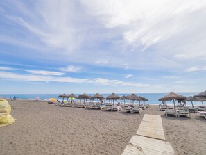Une plage bordée de rangées de chaises longues et d’ombrelles en chaume, une promenade en bois et l’océan en toile de fond.