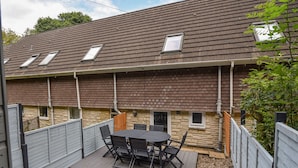 A covered patio with a table and chairs, a stone wall, and a wooden fence. - 51 Fernhill Heights (Bridport)