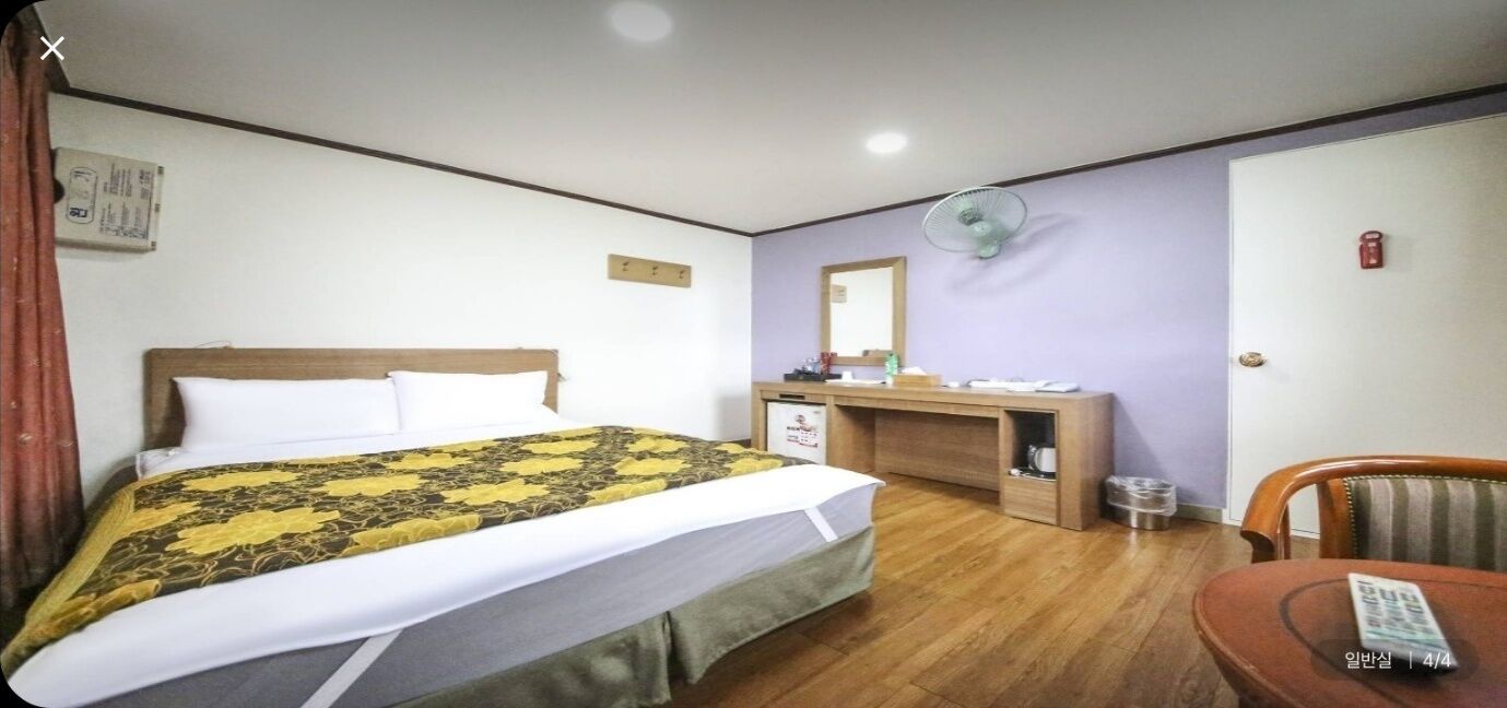 A hotel room with a bed, a desk, a chair, a desk fan, and a small table.