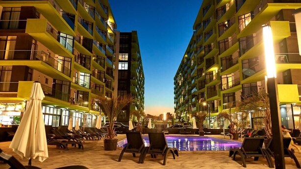 A nighttime view of a hotel with multiple high-rise buildings, a swimming pool, and outdoor seating areas with umbrellas.