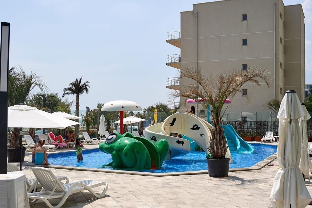 A pool area with slides and a large green water feature, surrounded by lounge chairs and umbrellas.