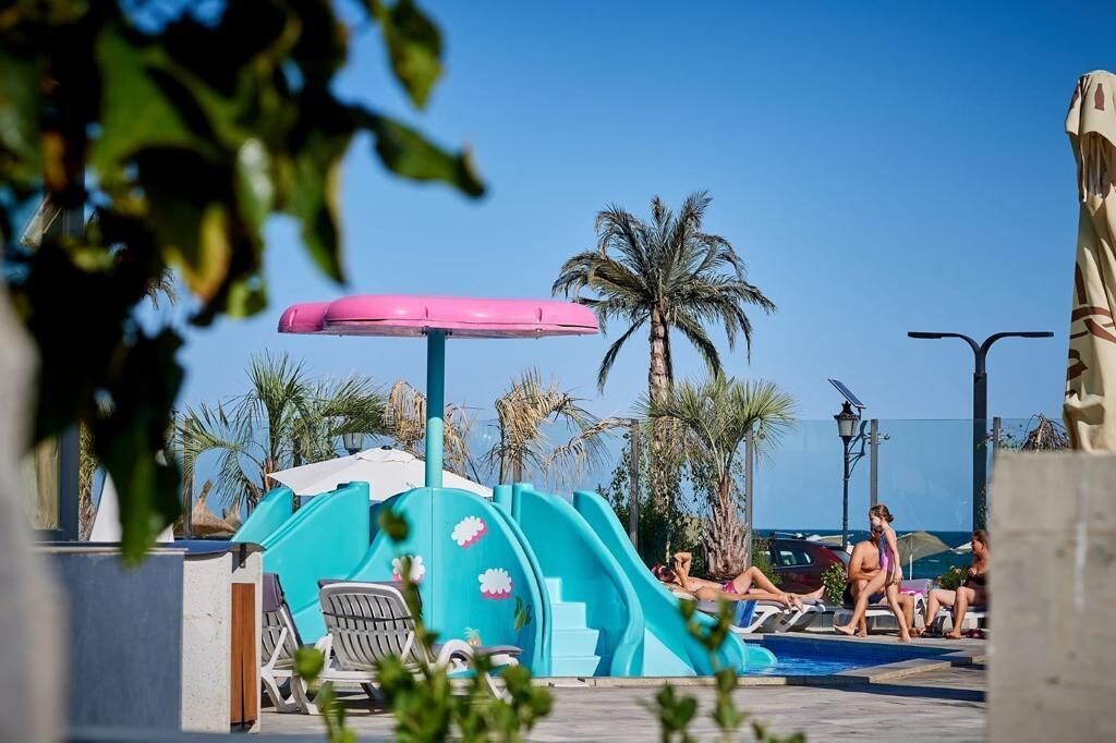 A pool area with a slide, lounge chairs, and palm trees.