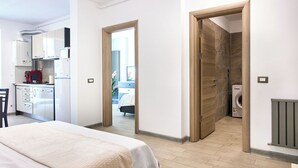 A modern hotel room with a bed, a kitchenette, a bathroom with a shower, and a view of the outside.