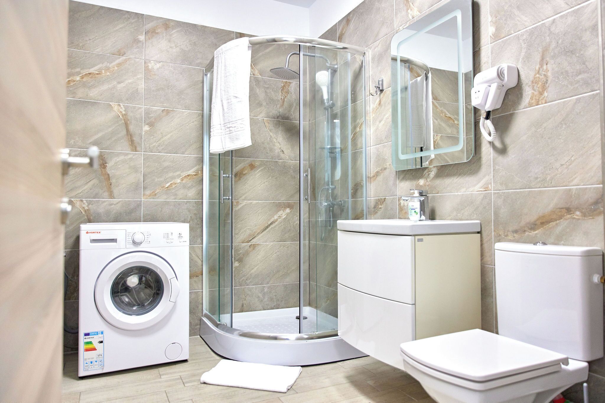 A modern bathroom with a glass-enclosed shower, a washing machine, a toilet, and a sink.
