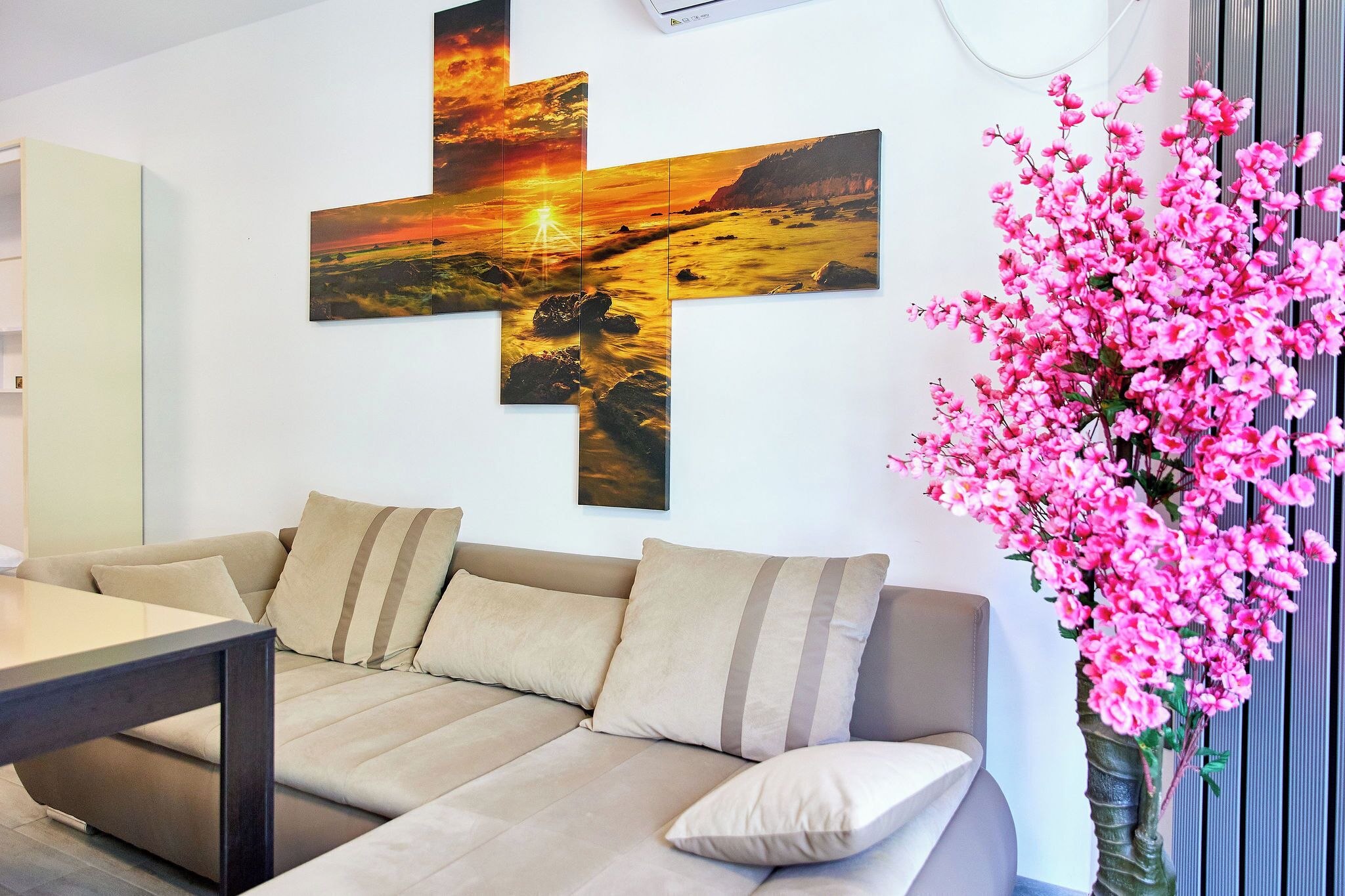 Een moderne woonkamer met een beige bank, een salontafel en een groot schilderij van een zonsondergang boven een landschap.