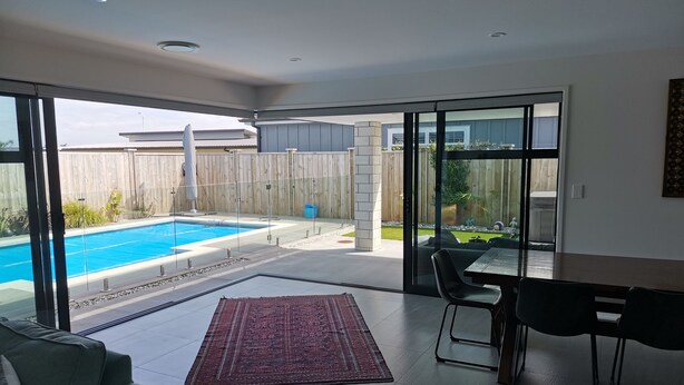 Ein modernes Wohnzimmer mit Pool, großen Schiebeglasfenstern, einem Essbereich und Blick auf den Garten.