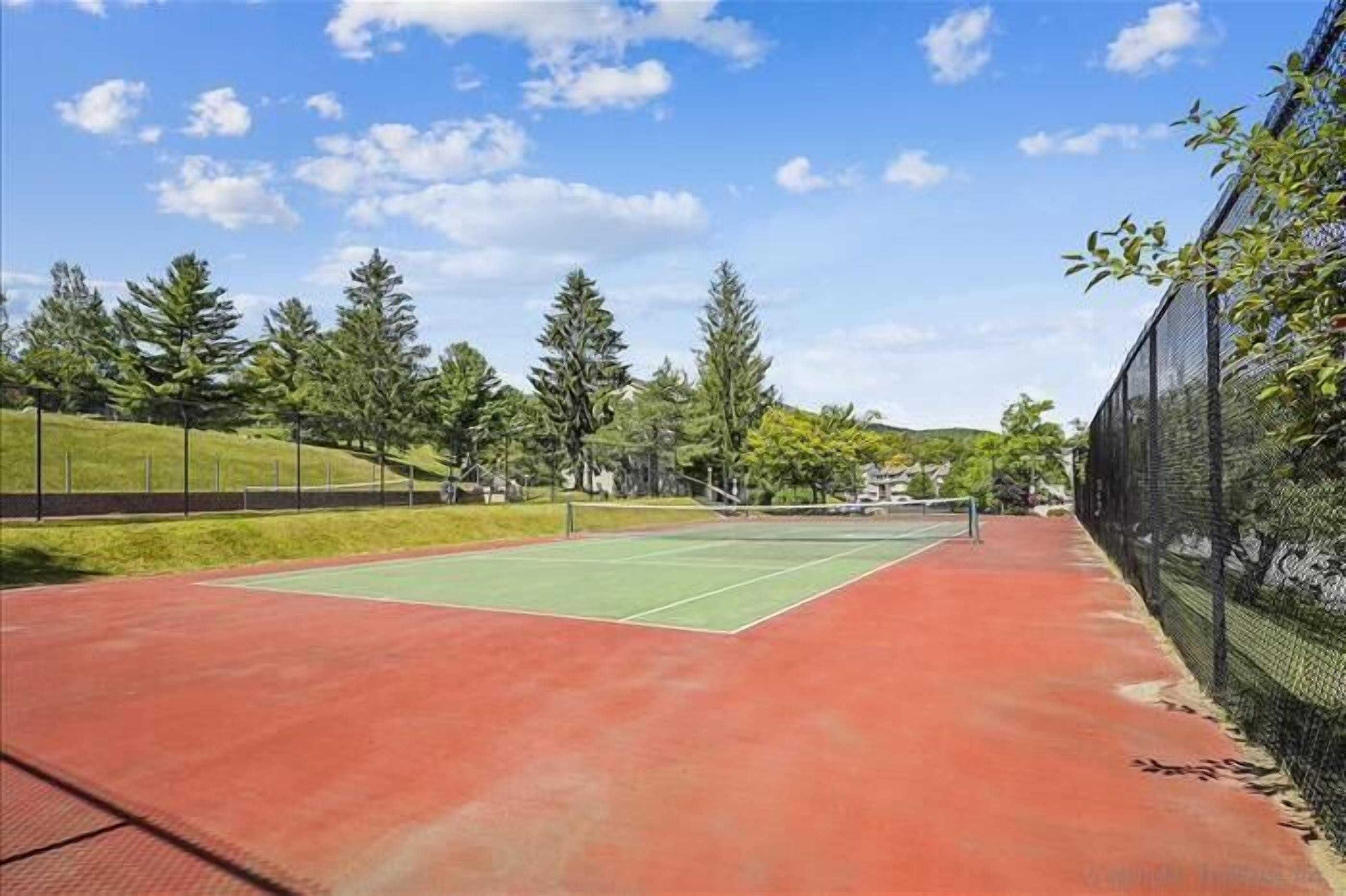 Een tennisbaan met rode ondergrond, omringd door bomen en een hek.