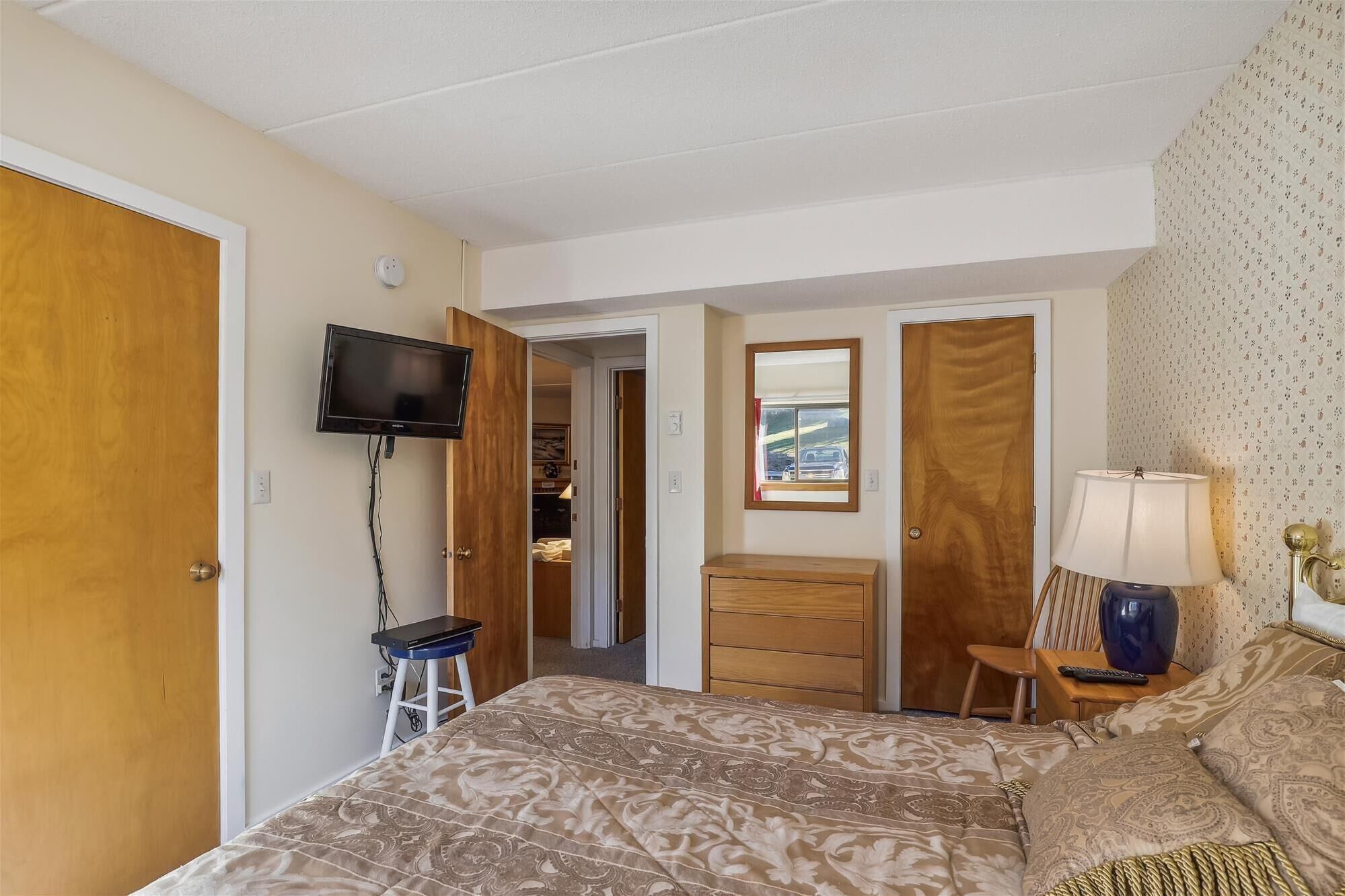 Une chambre à coucher comprenant un lit, un téléviseur fixé au mur, une commode, un miroir et une lampe.