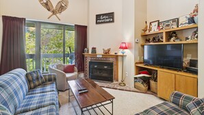 A cozy living room with a fireplace, a television, and a comfortable seating area. - Pinnacle D23 Condo | Pool, Hot Tub | Golf Nearby (Killington)