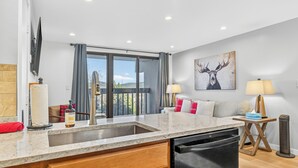 Een moderne keuken met een inbouwvaatwasser, een groot raam met gordijnen, en een eethoek met een tafel en stoelen.