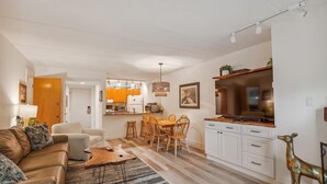 A modern living room with a sofa, coffee table, and a dining area with chairs and a table.