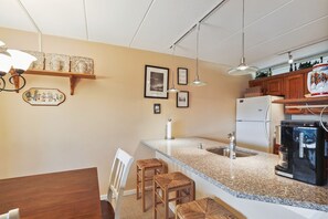 Une cuisine dotée d’un plan de travail en granit, de meubles blancs, d  ’un réfrigérateur et d’une machine à café.