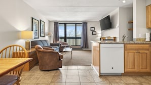 A modern living room with a dining area, kitchen, and a large window with curtains.