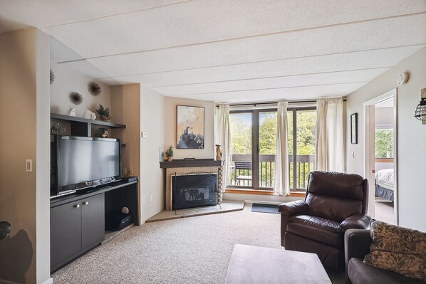 A living room with a fireplace, a television, and a comfortable seating area. - Pinnacle F08  Condo | Pool, Hot Tub | Golf Nearby (Killington)