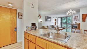 A modern kitchen with granite countertops, a stainless steel sink, wooden cabinets, and a chandelier. - Pinnacle B15 Condo | Pool, Hot Tub | Golf Nearby (Killington)