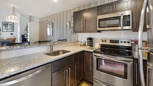 A modern kitchen with stainless steel appliances, granite countertops, and dark wooden cabinets. - Pinnacle C25 Condo | Pool, Hot Tub | Golf Nearby (Killington)