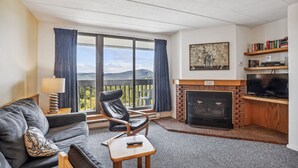 Ein Wohnzimmer mit Sofa, Sessel, kleinem Tisch, Kamin, Fernseher und Bücherregal.