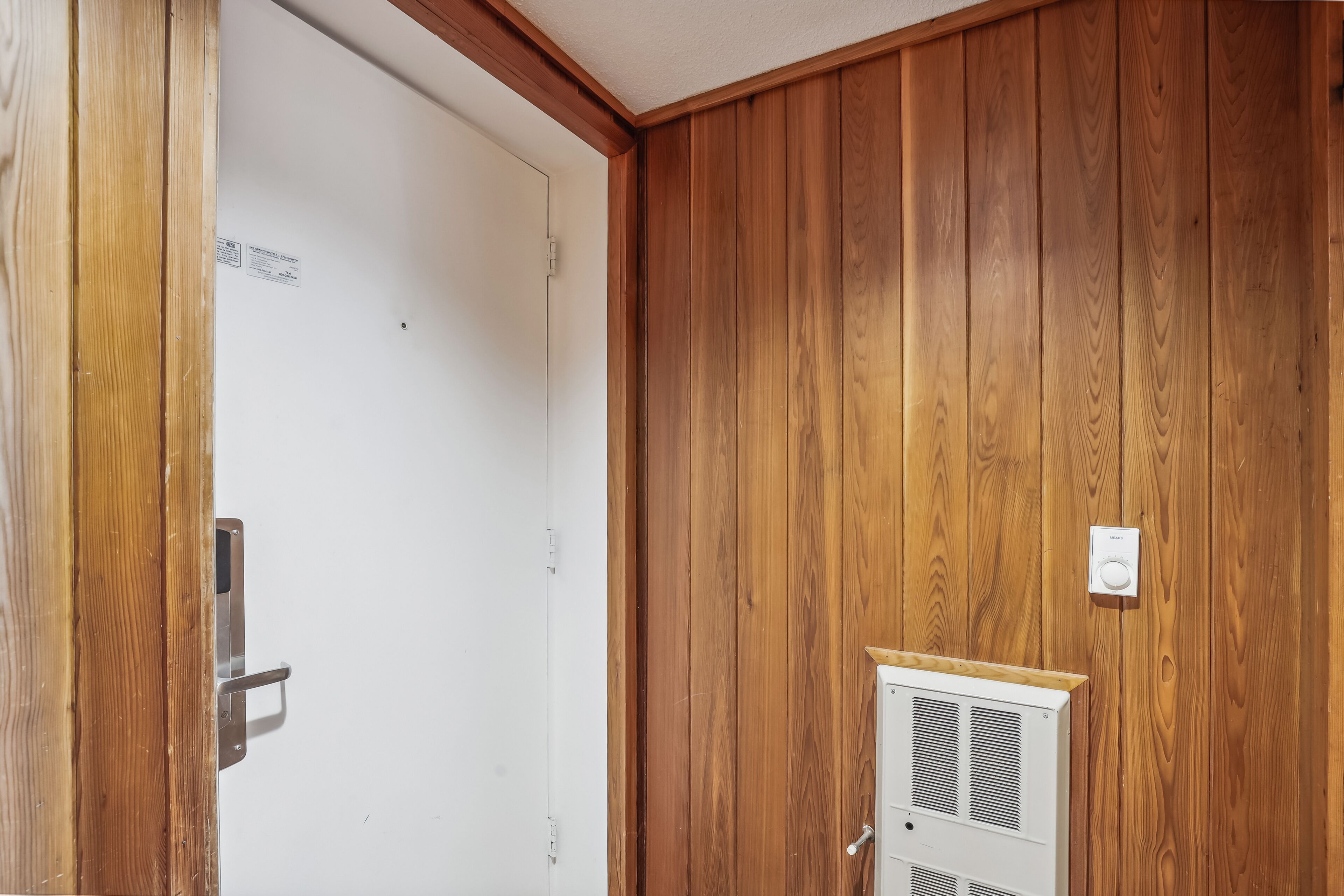 Een kamer met houten lambrisering, een witte deur en een thermostaat aan de muur.