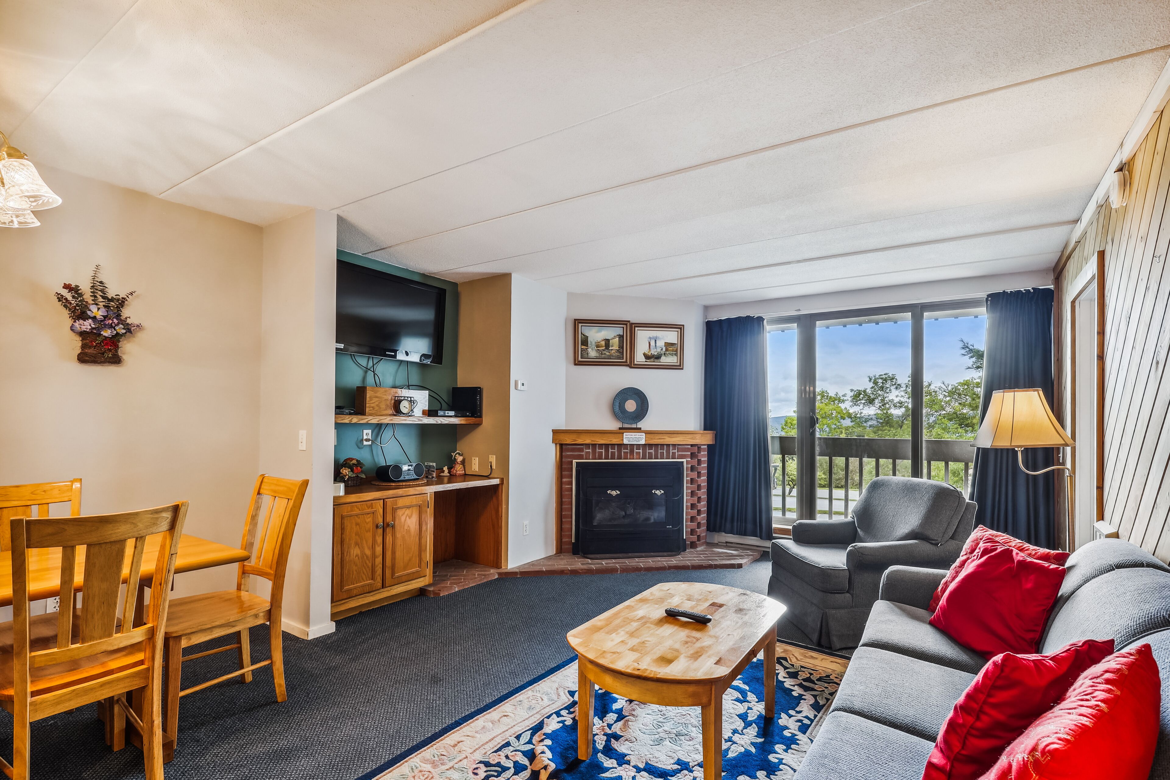 A living room with a fireplace, a dining area with wooden furniture, and a balcony with a view.