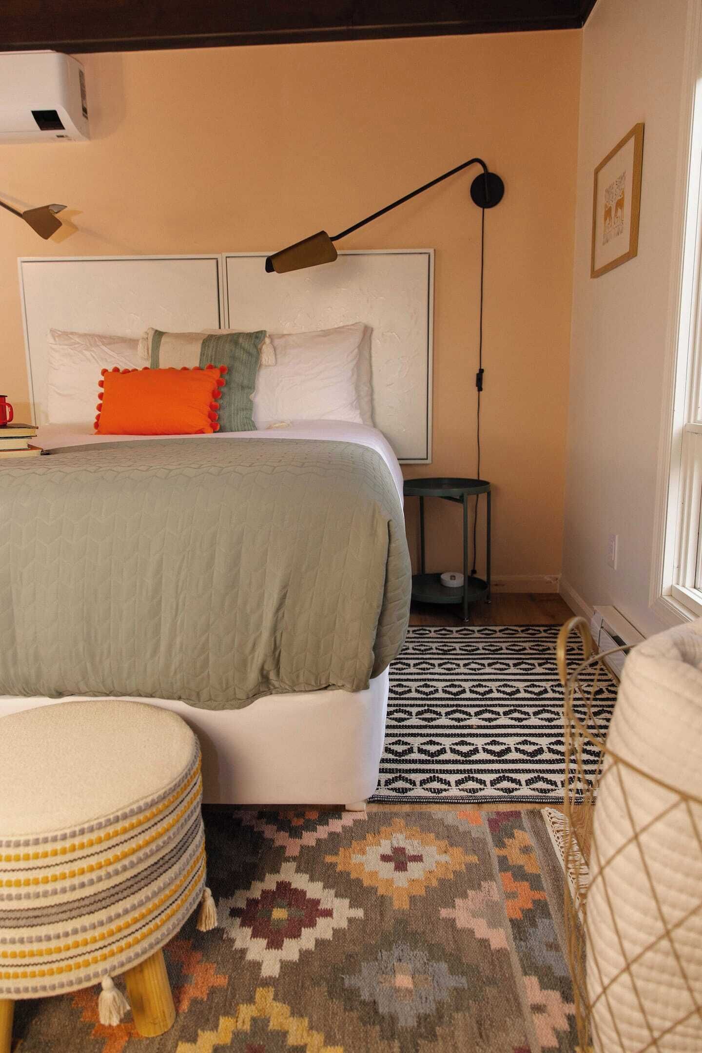 Un dormitorio con cama, mesita de noche, lámpara y alfombras estampadas.