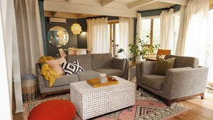 Un salon chaleureux avec un canapé gris, un pouf rouge et une table basse à motifs.