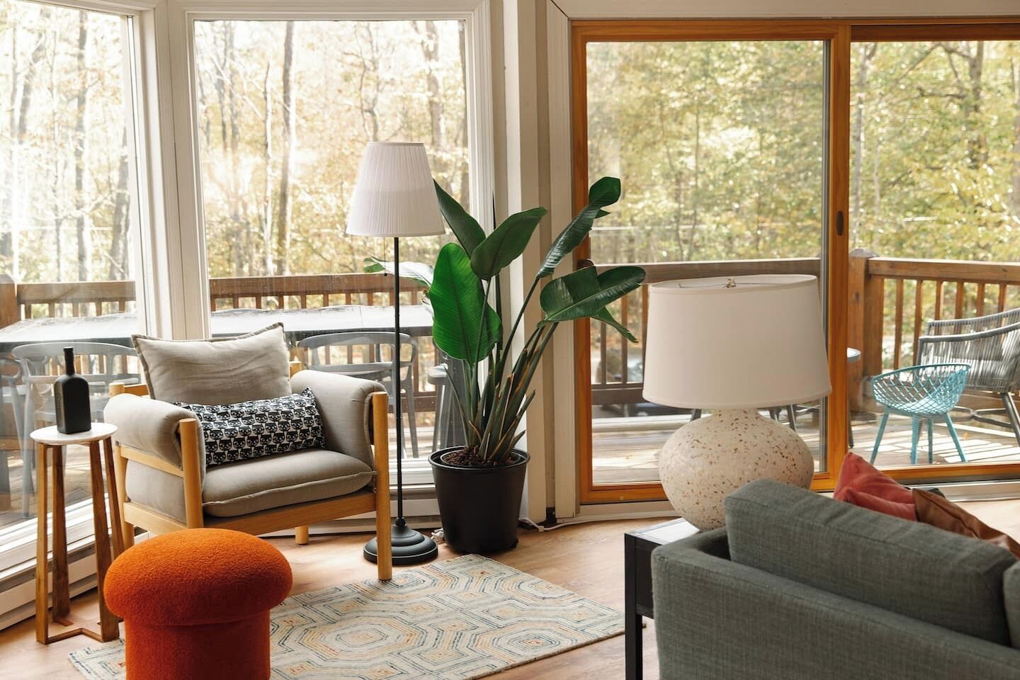 Un salon chaleureux avec un canapé, un fauteuil, une lampe sur pied, une plante en pot et une vue sur l’extérieur grâce à de grandes fenêtres.