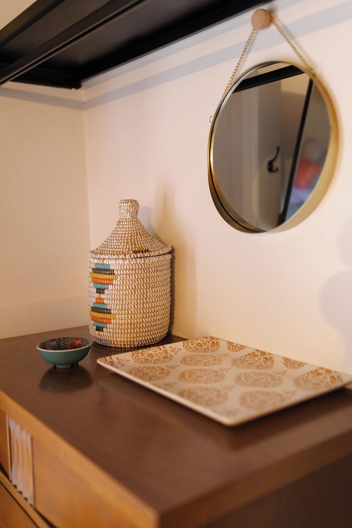 Een houten dressoir met een geweven mand, een kleine schaal en een decoratief bord.