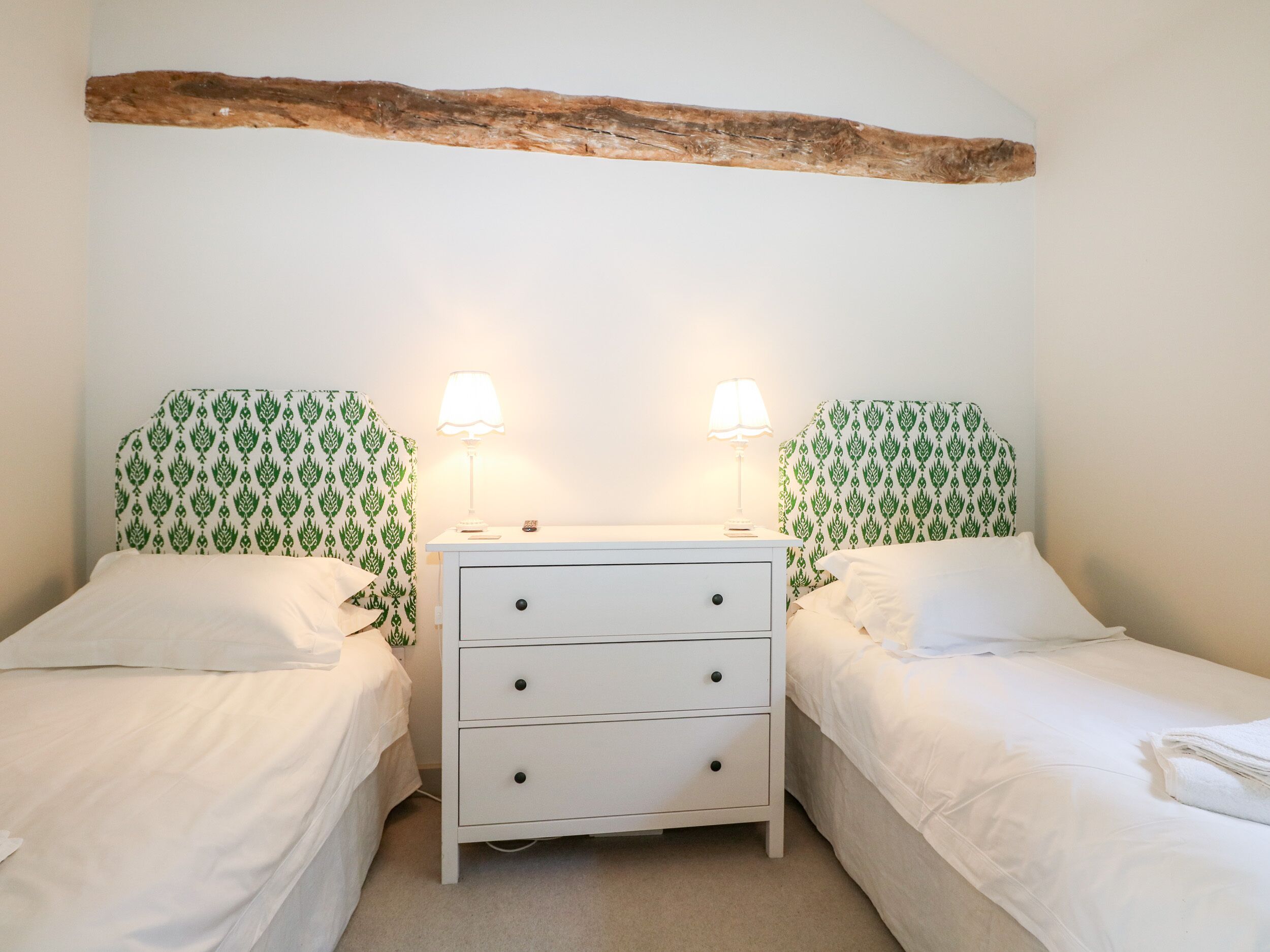 A bedroom with two single beds, a white dresser with drawers, and a wooden beam above the beds.