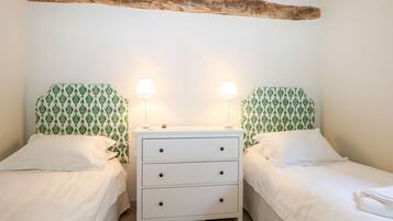 A bedroom with two single beds, a white dresser with drawers, and a wooden beam above the beds.