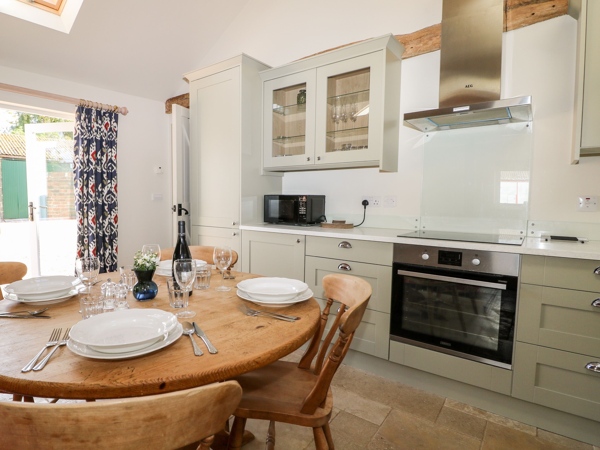A modern kitchen with white cabinets, a built-in oven, and a dining area with a wooden table set for four.