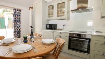 A modern kitchen with white cabinets, a built-in oven, and a dining area with a wooden table set for four.