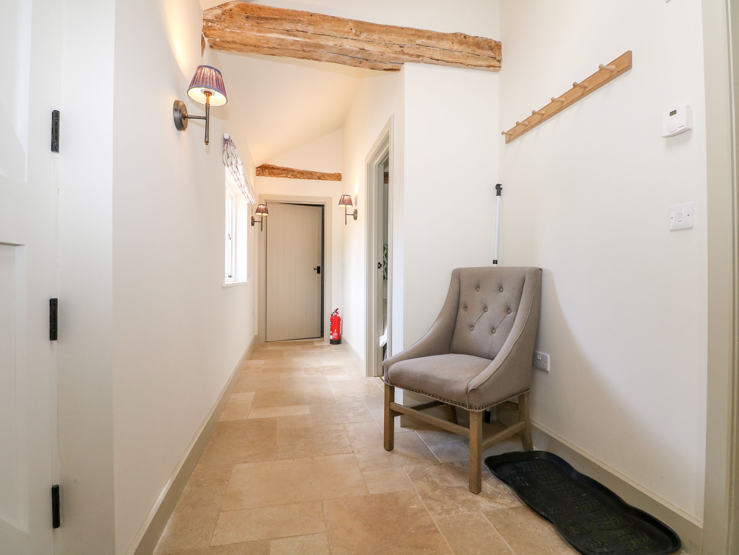 A hallway with a chair, a fire extinguisher, and a wooden beam ceiling.