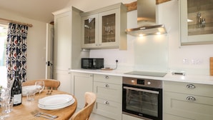 Een moderne keuken met witte kastjes, een ingebouwde magnetron, een oven en een eethoek met een houten tafel en stoelen.