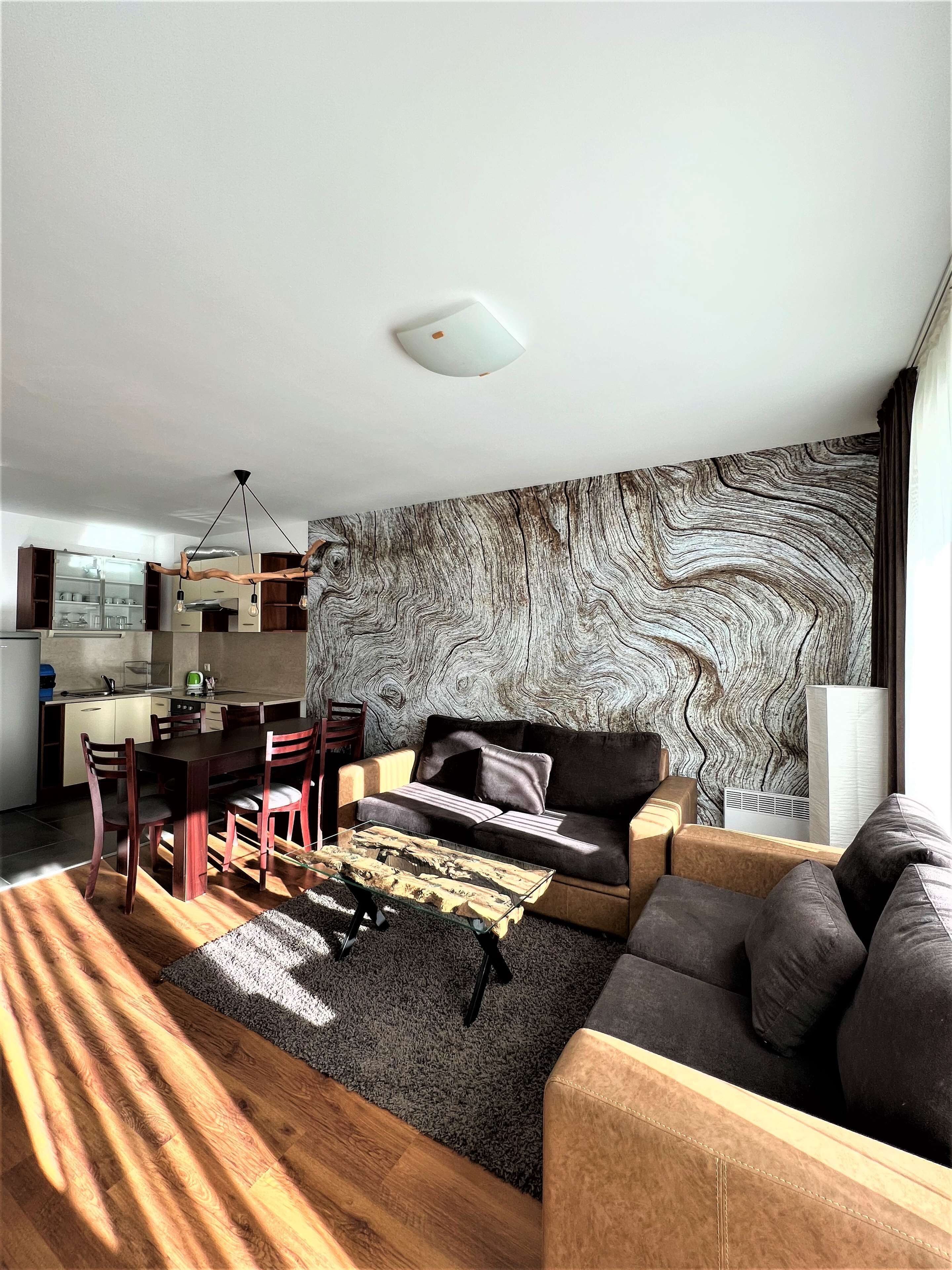 A modern living room with a wooden dining table, a sofa, and a large abstract wall mural.