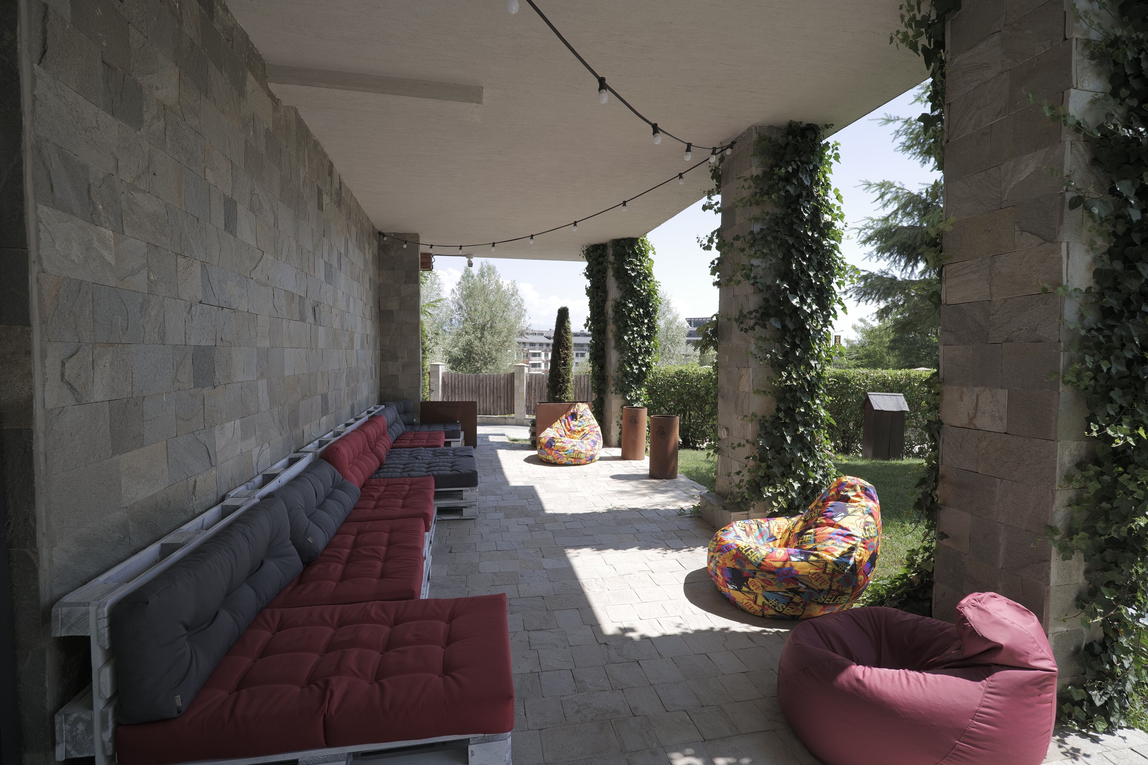 A covered outdoor seating area with stone walls, cushioned benches, and bean bags.