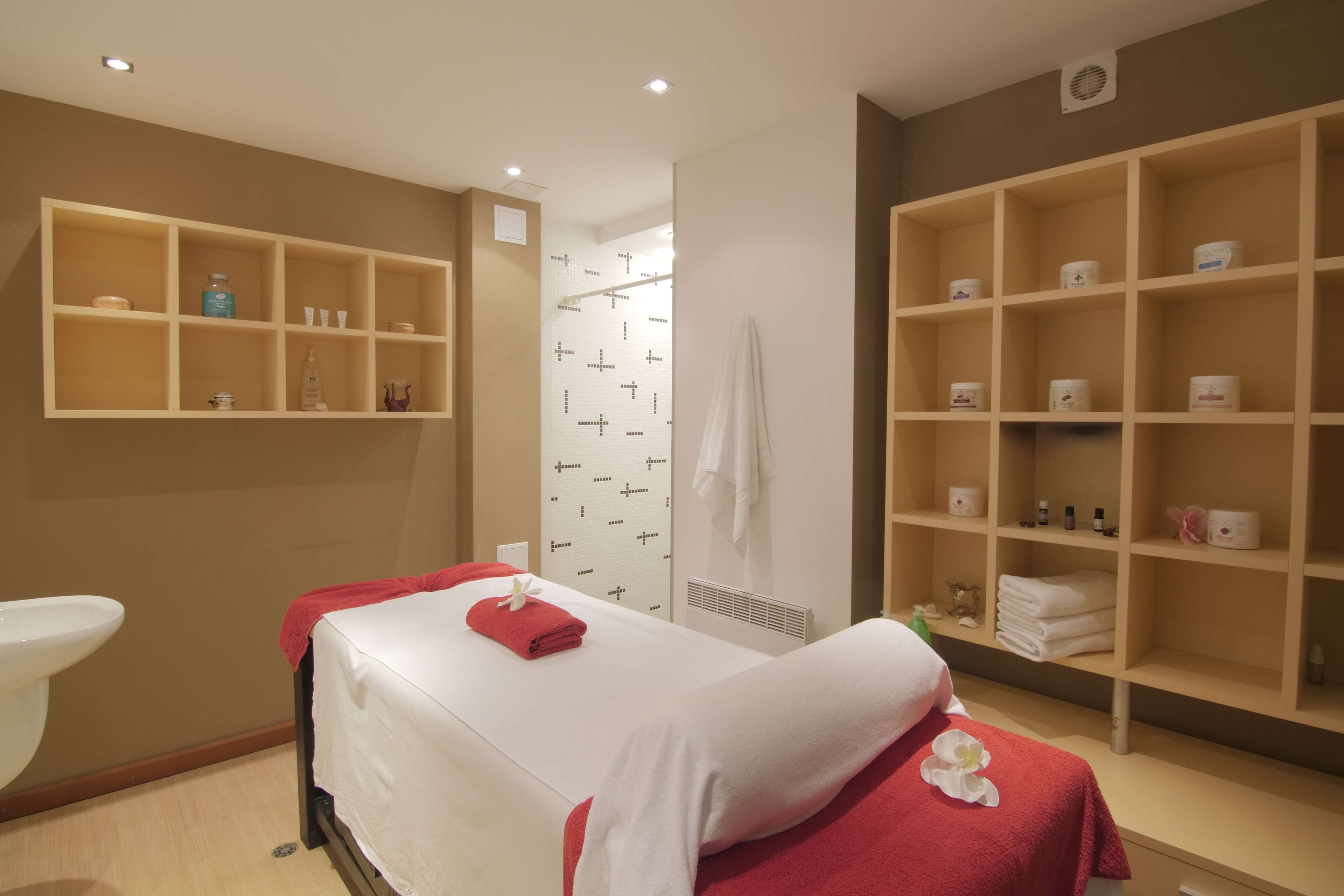 Een moderne spa-ruimte met een massagetafel, planken met toiletartikelen en een douchehoek.